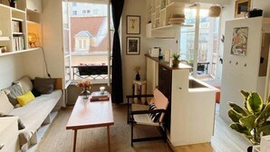 Una sala de estar acogedora con un sofá, una mesa de comedor y una zona de cocina con estantes y una lámpara colgante.