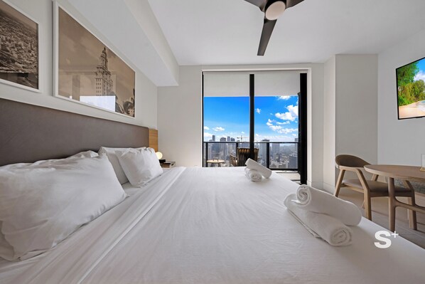 Une chambre d’hôtel moderne dotée d’un grand lit, offrant une vue sur la ville et comprenant un balcon avec une table et des chaises.