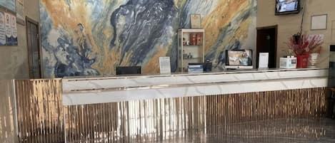 A reception area with a marble wall, a television, and a reception desk.