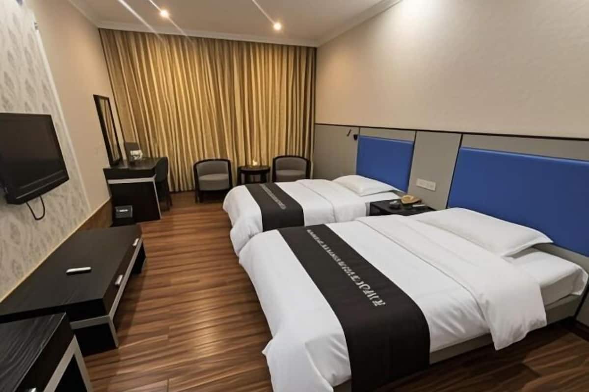 A hotel room with two beds, a desk, a chair, a TV, and a curtain.