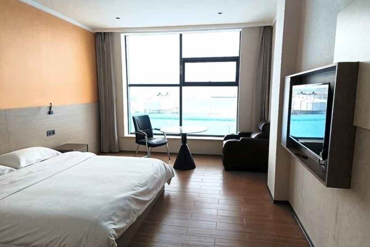 A hotel room with a bed, a TV, a chair, a small table, and a window with a view.