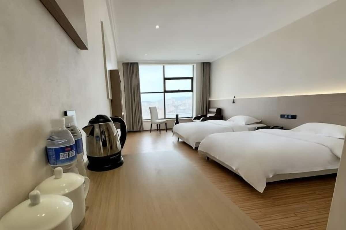A hotel room with two beds, a desk, a chair, a large window, and a view of the city.