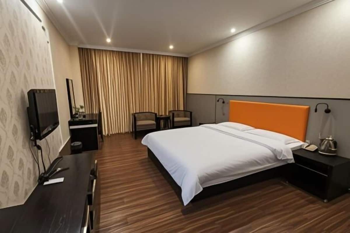 A hotel room with a bed, bedside table, chair, TV, and curtains.
