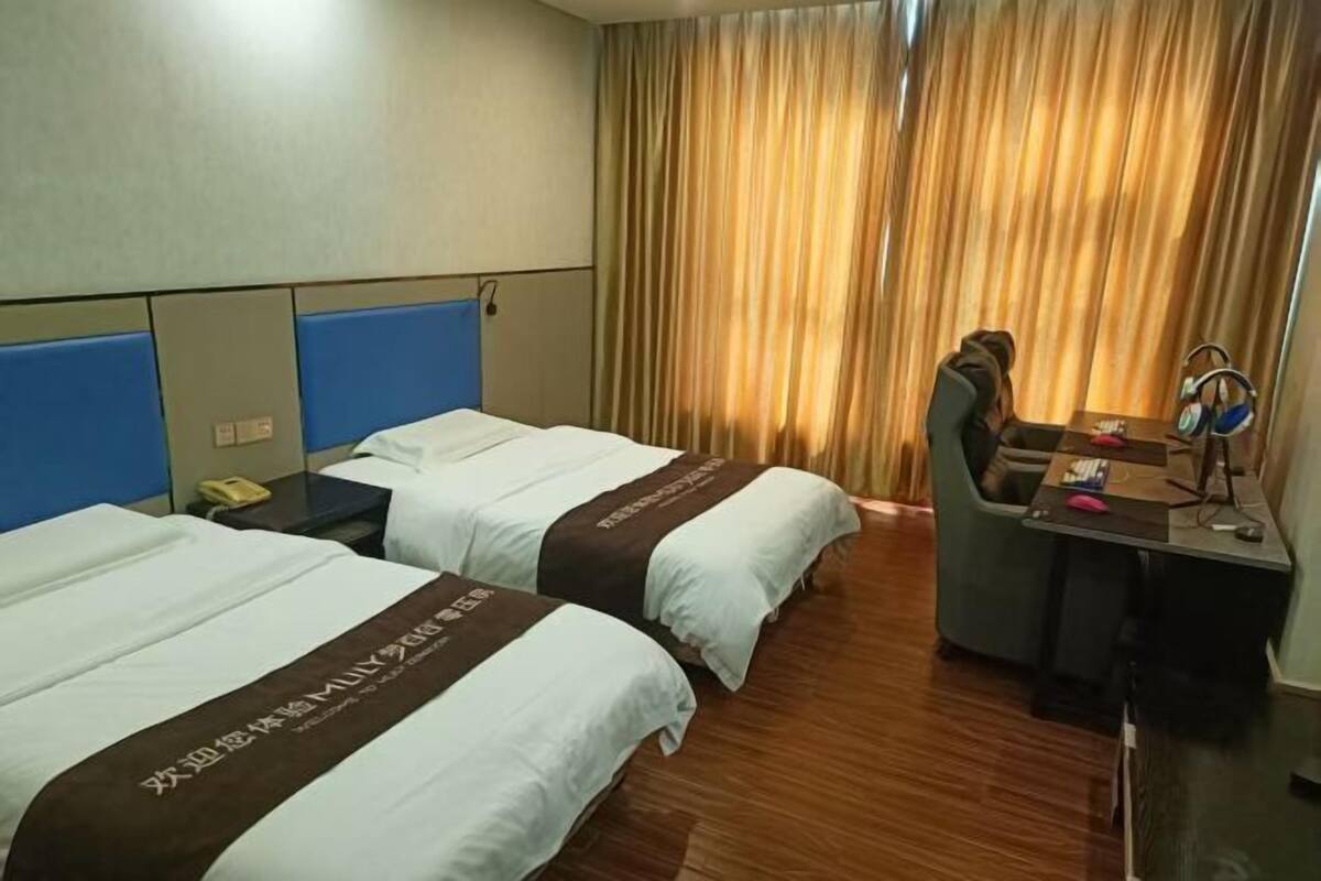 A hotel room with two beds, a desk, a chair, and a curtain.