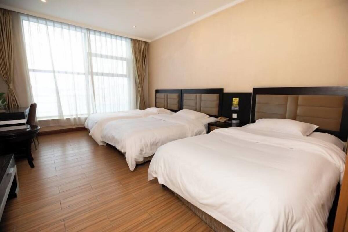 A hotel room with two beds, a desk, and a large window with curtains.