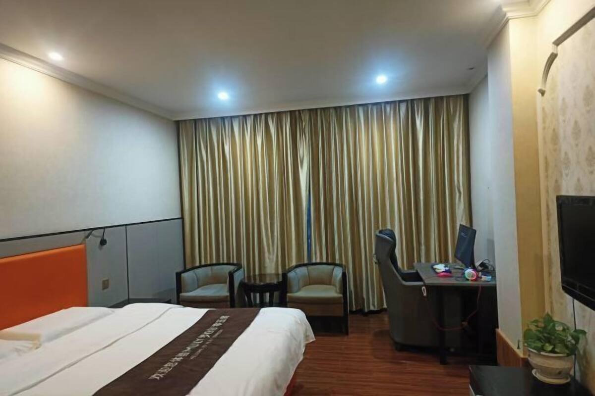 A hotel room with a bed, two chairs, a desk with a computer, and a TV.