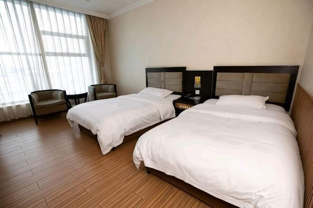 A hotel room with two beds, a desk, a chair, and a large window with curtains.