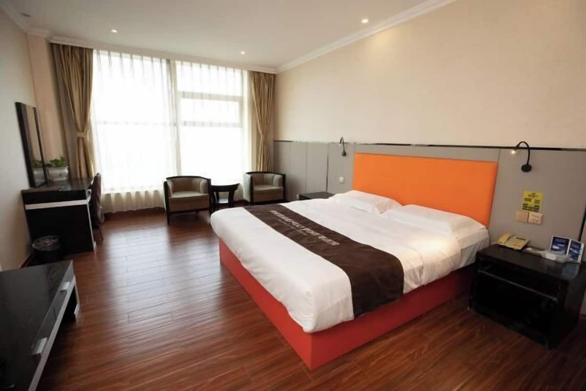 A hotel room with a large bed, a desk, a chair, and a TV.