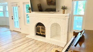 A living room with a white fireplace, a television mounted above it, and a piano.
