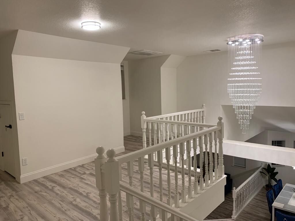 A spacious room with a white staircase, a chandelier, and a view of the upper floor.