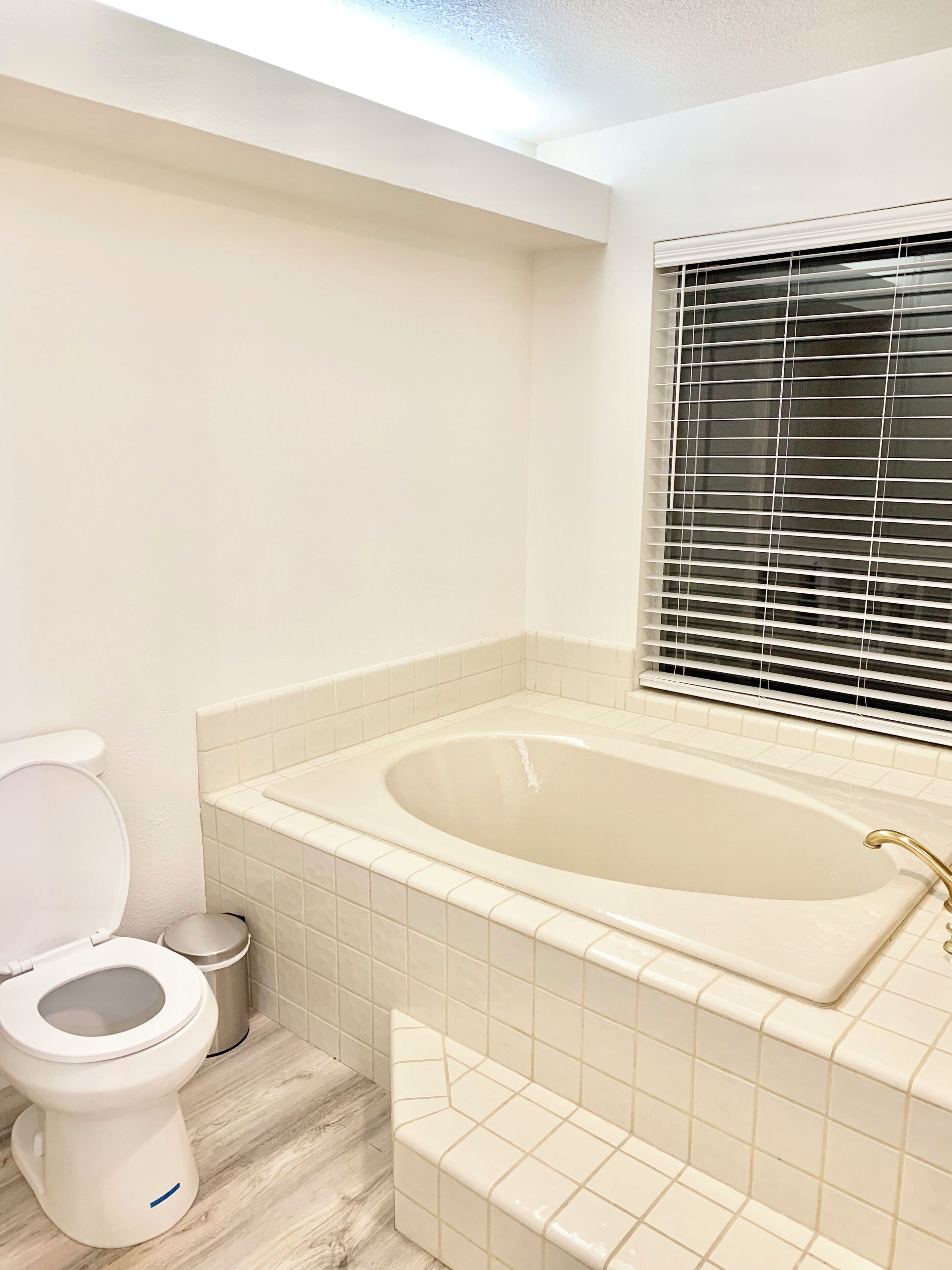 A bathroom with a toilet, a bathtub, and a window with blinds.