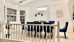 A dining area with a white railing, a chandelier, and a table set with blue chairs.