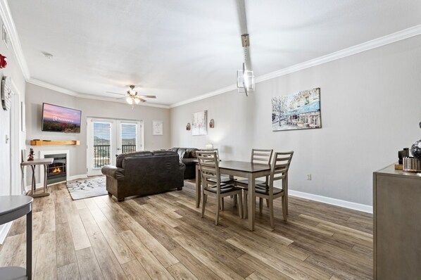 A spacious living room with a fireplace, a dining area with a table and chairs, a sofa, and a ceiling fan.