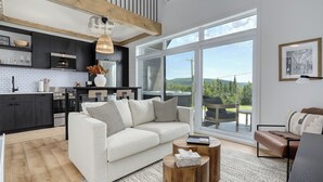 Un salon moderne avec un canapé blanc, une table basse et une vue sur l’extérieur grâce à de grandes fenêtres.