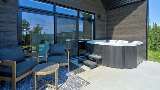 Un espace extérieur moderne, aménagé avec des sièges confortables, un jacuzzi, de grandes fenêtres et une vue sur le paysage environnant.
