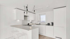 A modern kitchen with white cabinetry, a central island, bar stools, and a chandelier. - City Relay Radiant Chelsea Flat with City View (London)