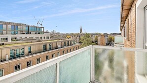 A high-rise building with multiple floors, large windows, and a view of a distant church spire. - City Relay Radiant Chelsea Flat with City View (London)