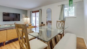 Una sala moderna con una mesa de comedor de vidrio, sillas de madera, un televisor de pantalla plana y un espejo grande.
