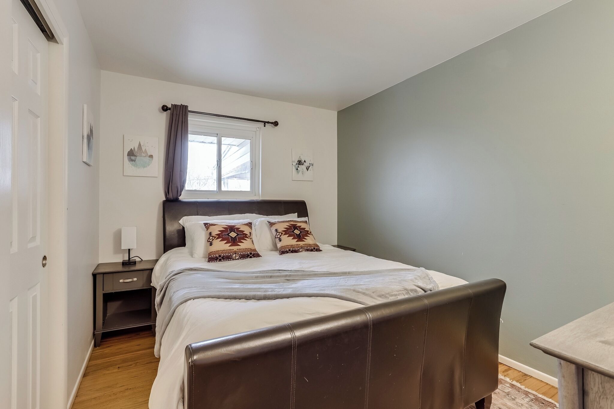 A bedroom with a bed, a nightstand, a window with curtains, and a wall with a picture.