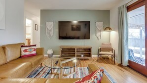Una sala de estar con un sofá de cuero, una mesa de centro de vidrio, un mueble de madera para entretenimiento y un televisor de pantalla plana grande.