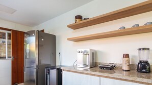 A modern kitchen with a stainless steel refrigerator, a coffee maker, a blender, and wooden shelves above the counter.