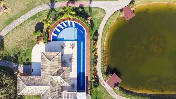An aerial view of a property with a swimming pool, a covered patio area, and a large pond.