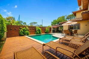 Un jardin avec une piscine, une terrasse en bois et du mobilier d’extérieur.