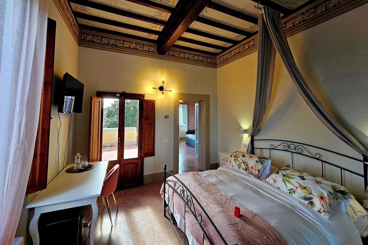 Une chambre à coucher comprenant un lit, un bureau, une chaise, un téléviseur et un plafond orné de poutres décoratives.