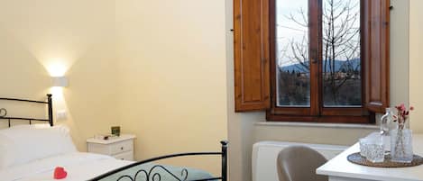 A bedroom with a bed, bedside table, lamp, window, radiator, and a desk with a chair.
