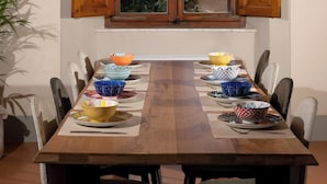A dining table with multiple bowls and plates, set against a wall with a window and wooden shutters.