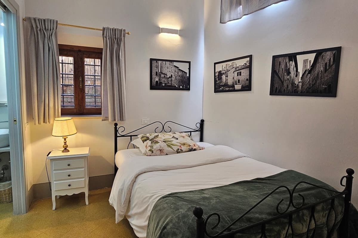 Une chambre à coucher comprenant un lit, une table de chevet, une lampe, des rideaux et trois photographies en noir et blanc accrochées au mur.