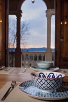 Una mesa de comedor con un tazón y platos, un tenedor, y una vista de un paisaje montañoso a través de una ventana arqueada.