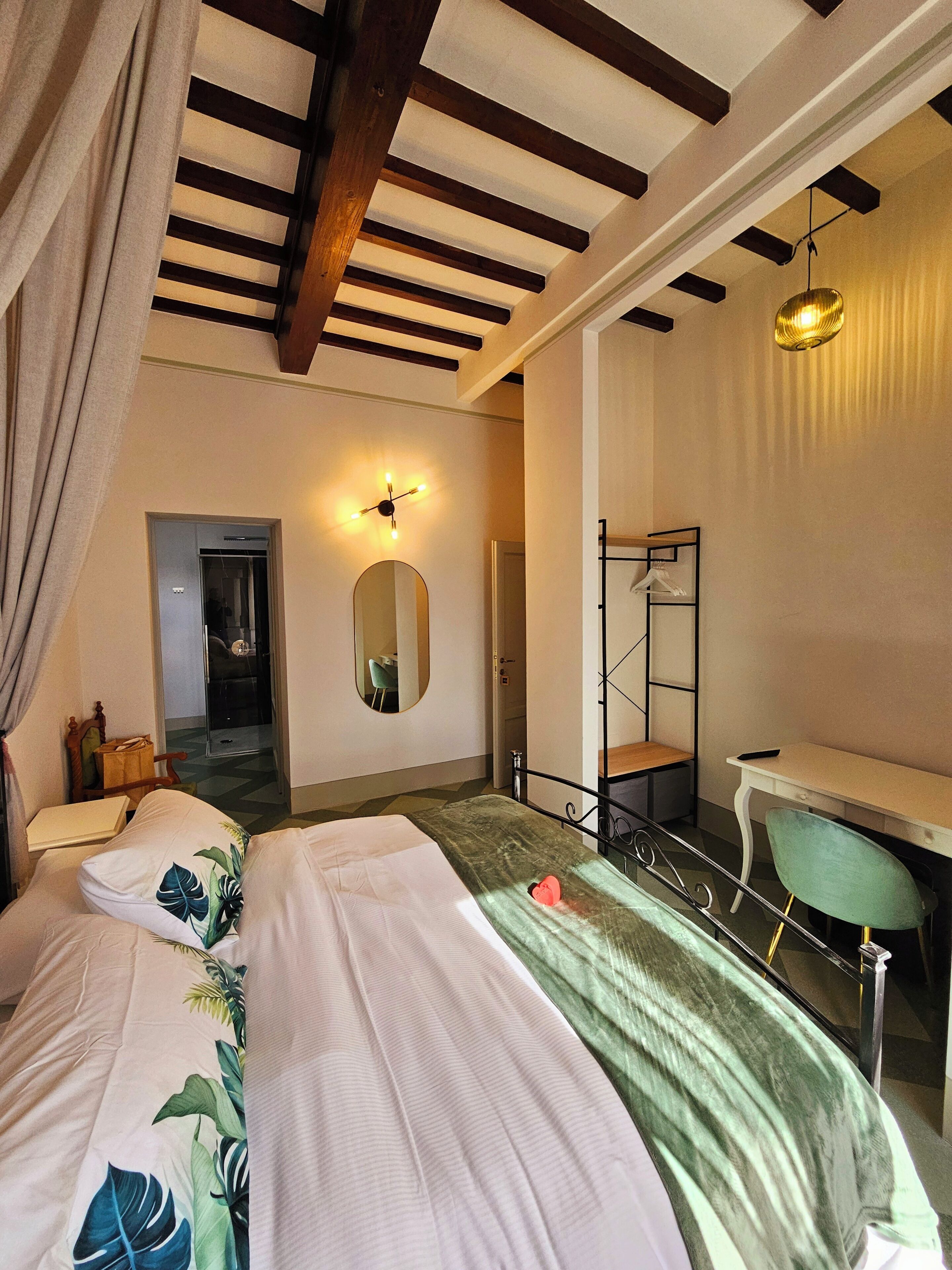 A bedroom with a bed, a desk, a mirror, and a door leading to another room.