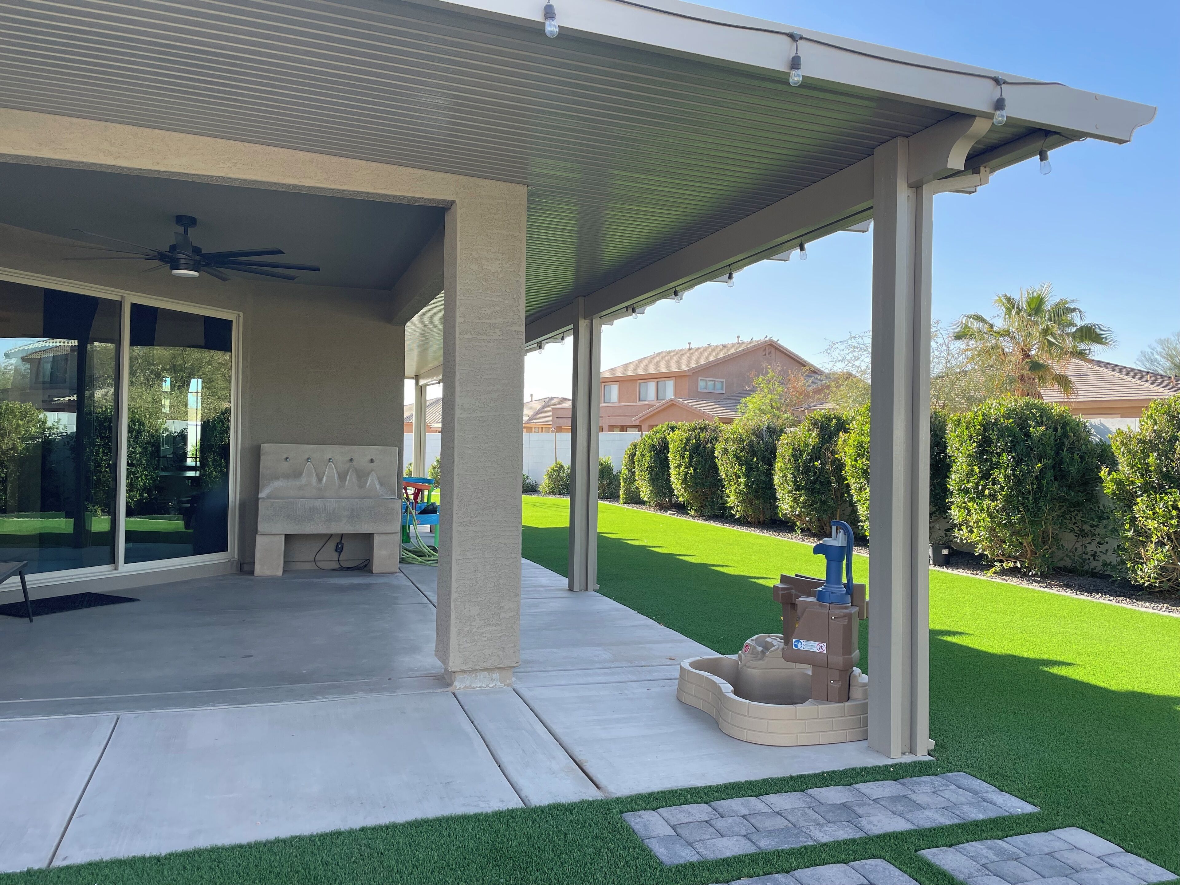 Un'area patio coperta con ventilatore a soffitto, una panca e una fontana.