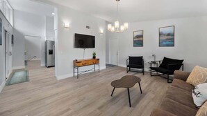 Ett modernt vardagsrum med en platt-TV, ett bord i trä, en brun lädersoffa och en svart fåtölj.