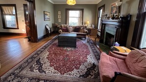 Un salon spacieux doté de planchers en bois franc, d’un grand tapis à motifs, d’un canapé, d’un fauteuil et d’une cheminée.