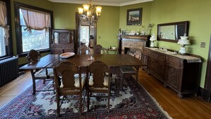 Une salle à manger avec une table en bois, des chaises, un lustre, une cheminée et un miroir au mur.