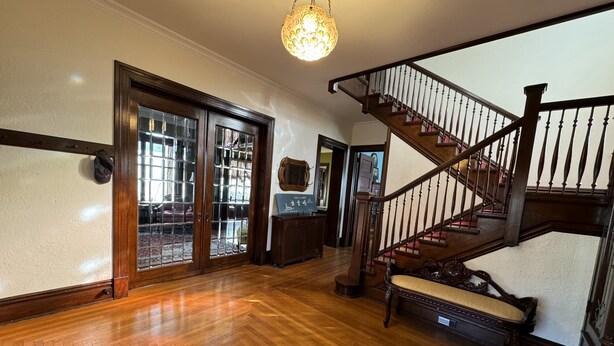 Un hall d’entrée spacieux, agrémenté d’un escalier en bois, d’un lustre et donnant sur un salon grâce à des portes vitrées.