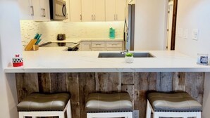Une cuisine moderne avec des meubles blancs, un plan de travail blanc et un coin bar en bois équipé de tabourets.
