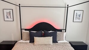 Un dormitorio moderno con cama con dosel, dos mesitas de noche y cabecera con luz trasera roja.