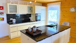 A compact kitchen with white cabinets, a black countertop, and a small island. There is a window with a curtain, a clock on the wall, and a kettle on the countertop. - Concierge, Lake Thun/Alps Scenic Views by SwissHut (Sigriswil)