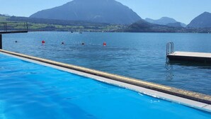 A swimming pool with clear blue water, a diving board, and a mountain in the background. - Concierge, Lake Thun/Alps Scenic Views by SwissHut (Sigriswil)