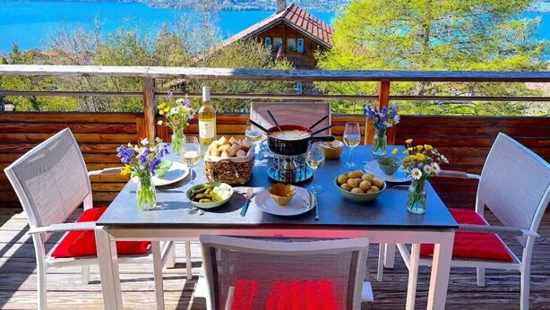 A dining table set outdoors with a mountain view, a wooden deck, and a rustic house in the background. - Concierge, Lake Thun/Alps Scenic Views by SwissHut (Sigriswil)