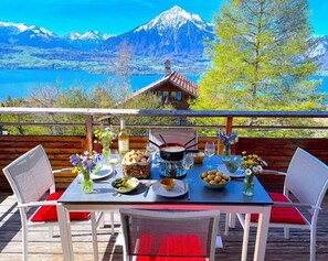 A dining table set outdoors with a mountain view, a wooden deck, and a rustic house in the background. - Concierge, Lake Thun/Alps Scenic Views by SwissHut (Sigriswil)