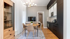 A modern kitchen with dark cabinetry, a dining area with a round table and chairs, and a TV mounted above the counter. - Luxury 2BD apartment in City Center (Tallinn)