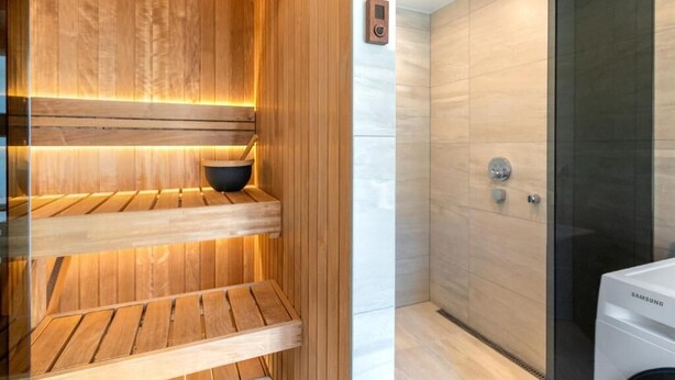 A modern bathroom with a wooden sauna, a glass shower enclosure, and a Samsung washing machine. - Luxury 2BD apartment in City Center (Tallinn)