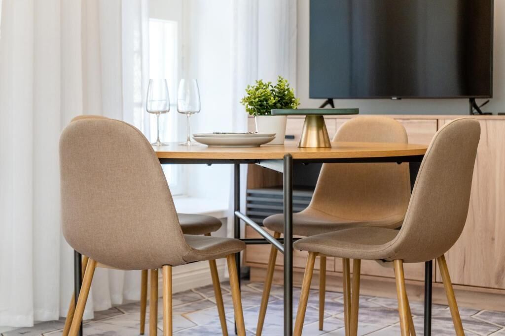 Un comedor con una mesa de madera, dos sillas color beige, una pequeña planta en maceta y un televisor de pantalla plana montado en la pared.