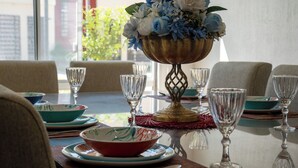 Une table à manger dressée avec des assiettes, des bols et des verres à vin, et un vase décoratif rempli de fleurs placé au centre.