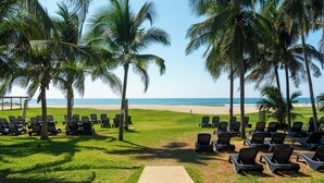 Un espace de détente aménagé au bord de la plage, avec des rangées de chaises longues et des palmiers, qui s’étend jusqu’à l’océan.