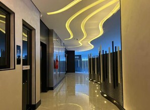 Un pasillo moderno de hotel con piso reflectante, diseño de lámpara de techo curvo y vista de la ciudad por la noche.